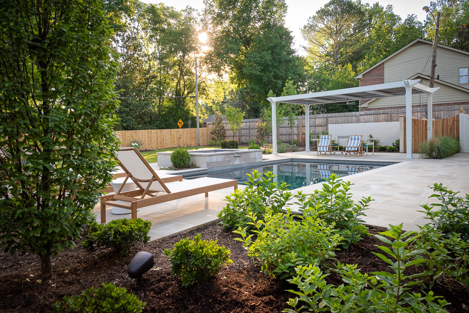 A designed backyard space featuring a pool, pool chairs, a pergola, and green landscaping