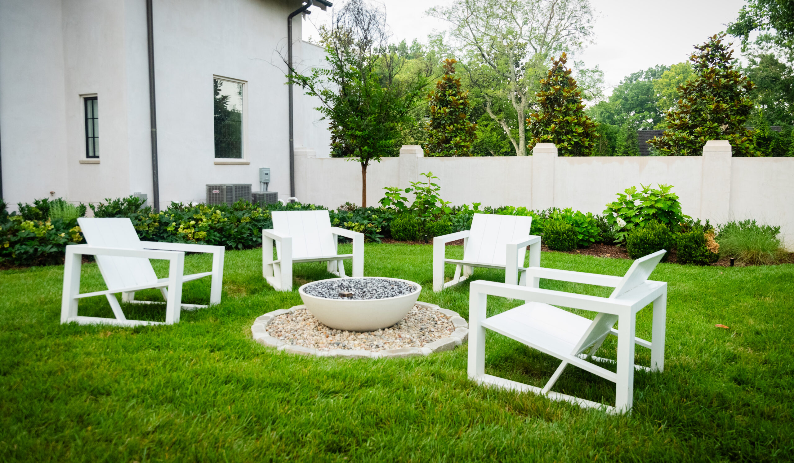 A backyard of a Nashville home that has a stone fire pit and 4 white chairs surrounding it